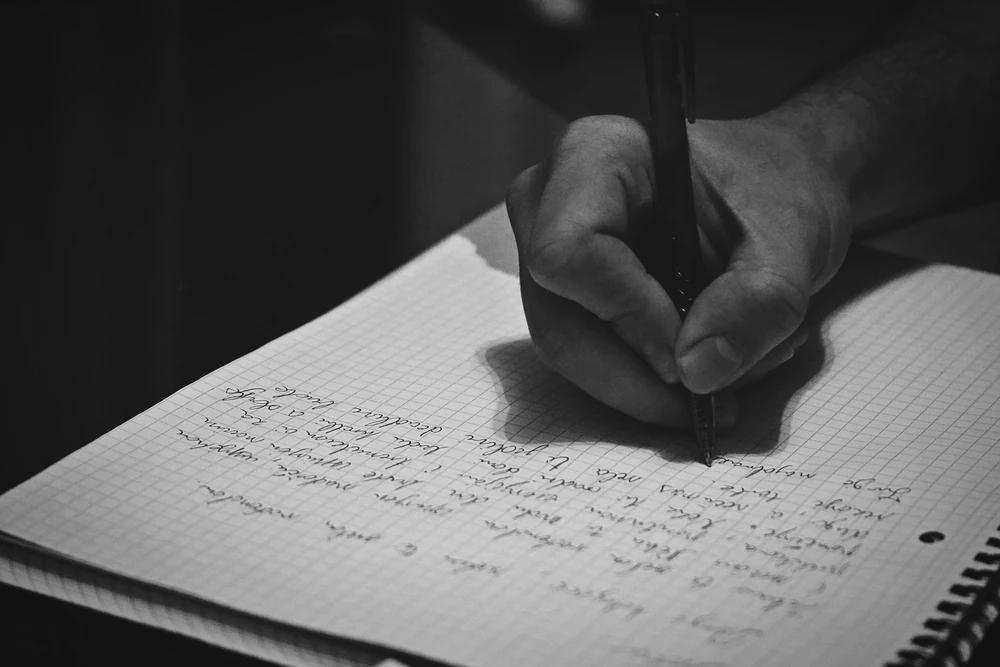Een hand schrijft met een pen in een notitieboek.