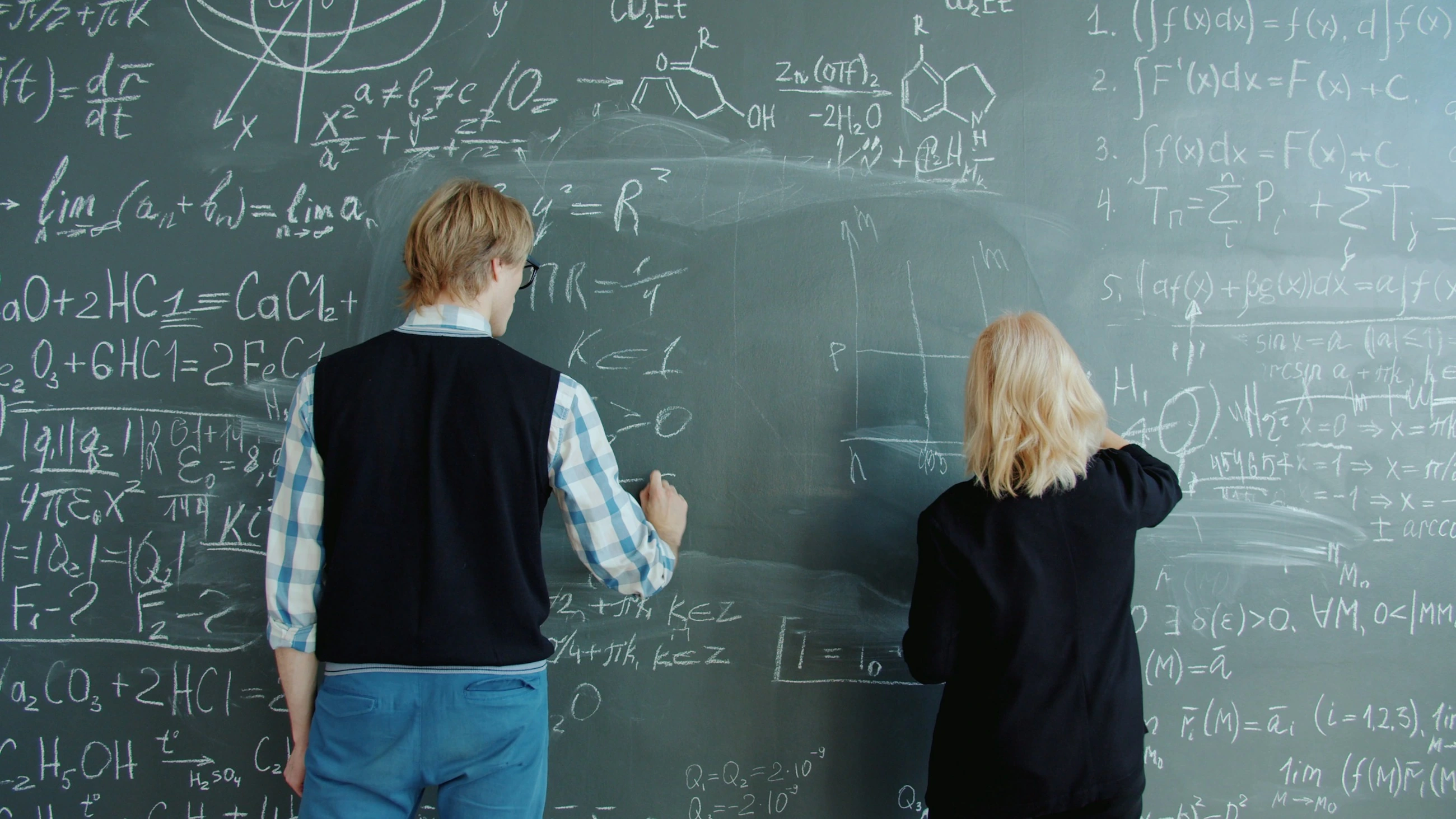 Twee mensen werken met wiskundige formules op een krijtbord.