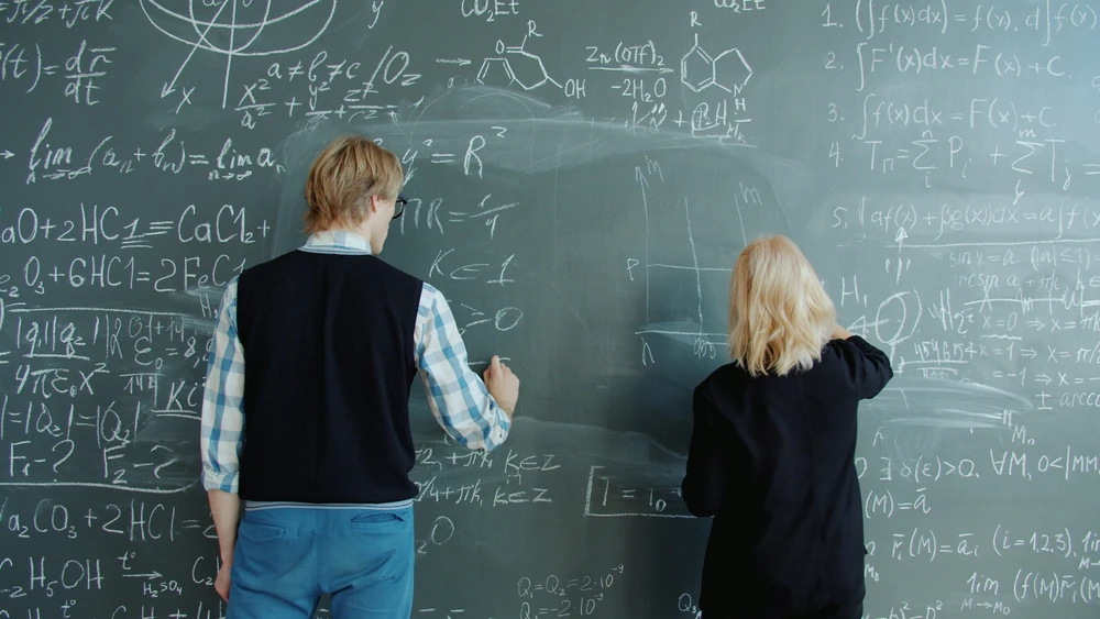 Twee mensen werken met wiskundige formules op een krijtbord.